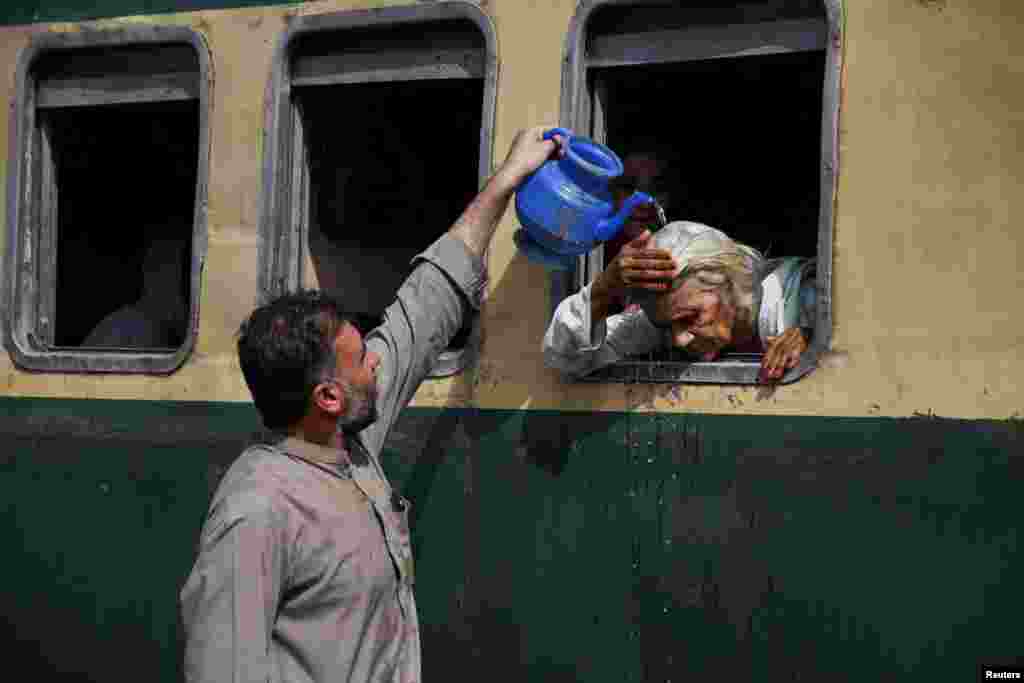 A man pours water on a passenger&#39;s head to cool off during a hot and humid day at the Hyderabad Railway Station in Hyderabad, Pakistan.