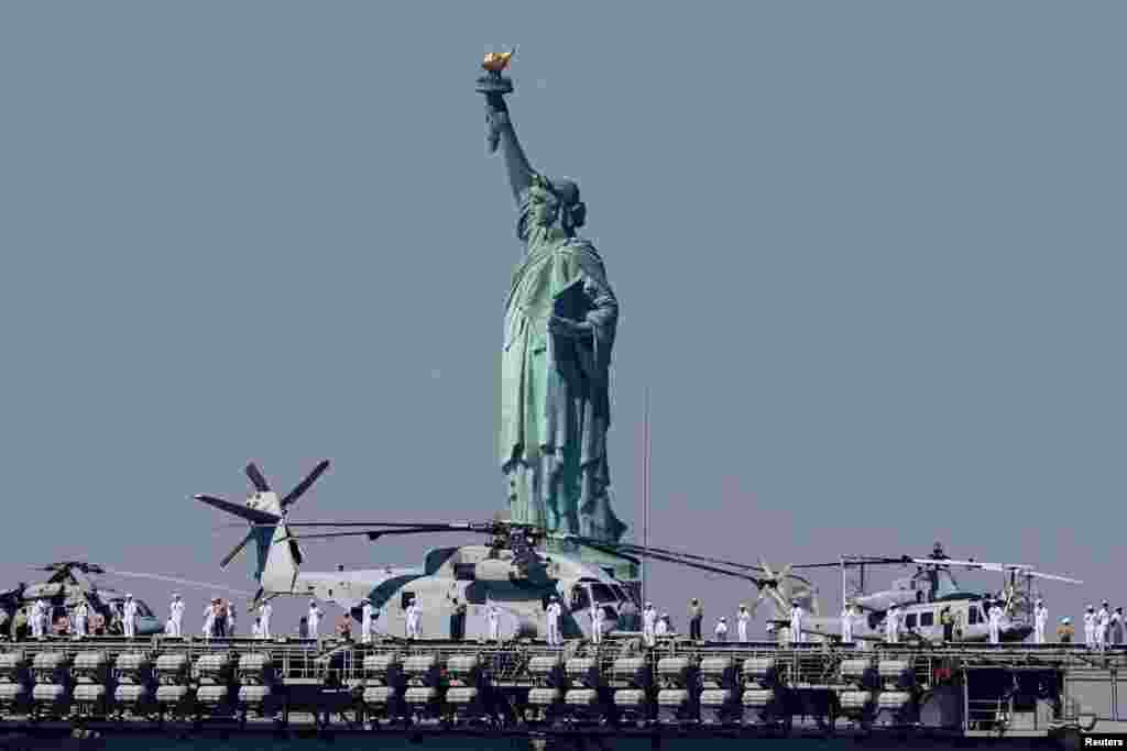 Sailors and Marines line the deck of the USS Bataan (LHD-5) Wasp-class amphibious assault ship, as it passes by the Statue of Liberty arriving in New York Harbor during the parade of ships to kick off &quot;Fleet Week 2024&rdquo; in New York City.