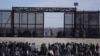 FILE - Migrants who crossed the border from Mexico into the US wait next to the US border wall where US Border Patrol agents stand guard, seen from Ciudad Juarez, Mexico, March 30, 2023. 