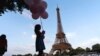 ILUSTRASI - Seorang turis memegang seikat balon, saat berjalan bersama keluarganya di tepian sungai Seine depan menara Eiffel Tower, Paris, 29 Juli 2024.