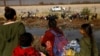 FILE - Migrants seeking asylum in the United States gather on the banks of the Rio Bravo as the Texas National Guard blocks the crossing at the border between the United States and Mexico, as seen from Ciudad Juarez, Mexico, Dec. 5, 2023. 