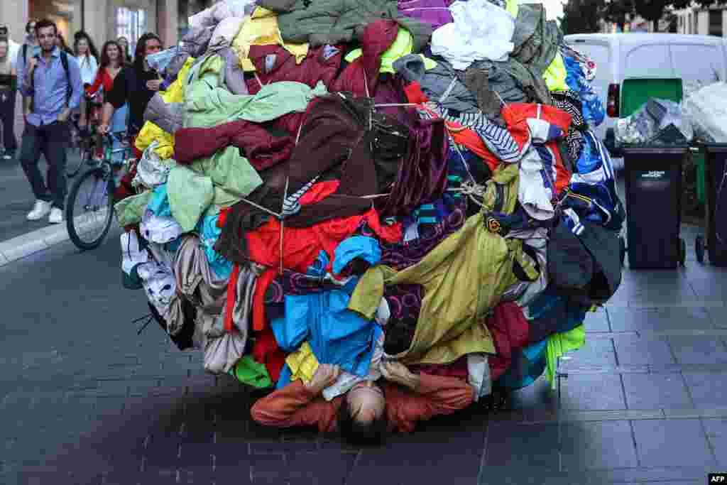 Actor and director Dorian Chavez (C) pushes a ball covered by clothes as part of a performance called &quot;Sisypholia&quot; denouncing the &quot;absurdity&quot; of overconsumption in Toulouse, southwestern France, Oct. 5, 2022, during the &quot;Biennale des arts vivants de Toulouse.&quot;