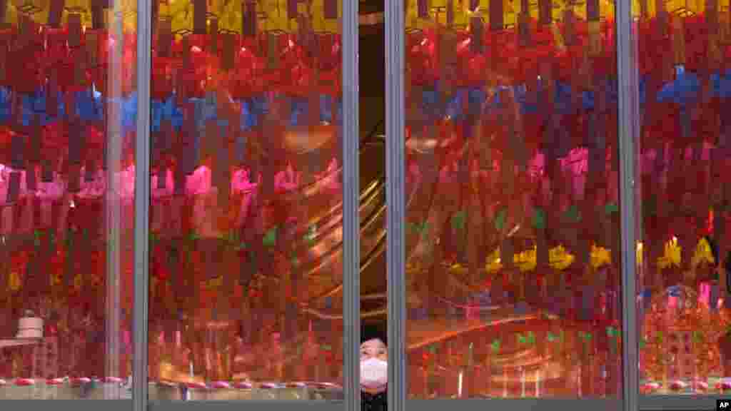 A woman wearing a face mask opens the window which reflects lanterns displayed for upcoming Buddha&#39;s birthday celebration at Jogyesa temple in Seoul, South Korea.