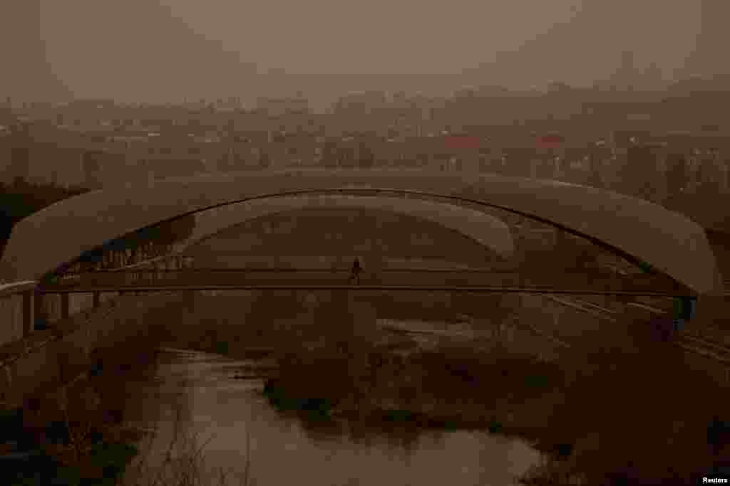 A person wearing a protective mask crosses a bridge as storm Celia blows sand from the Sahara desert over Madrid, Spain.