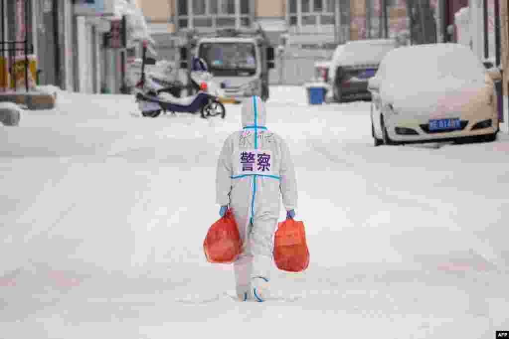 A police officer wearing personal protective equipment carries food and daily supplies that will be distributed to those living in a restricted residential area because of the spread of COVID-19 in Manzhouli in China&#39;s northern Inner Mongolia region.