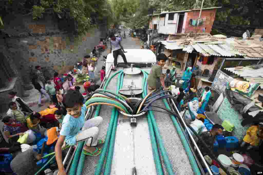 Residents use hoses to collect drinking water from a tanker truck during a hot summer day in New Delhi, India, May 3, 2022. 