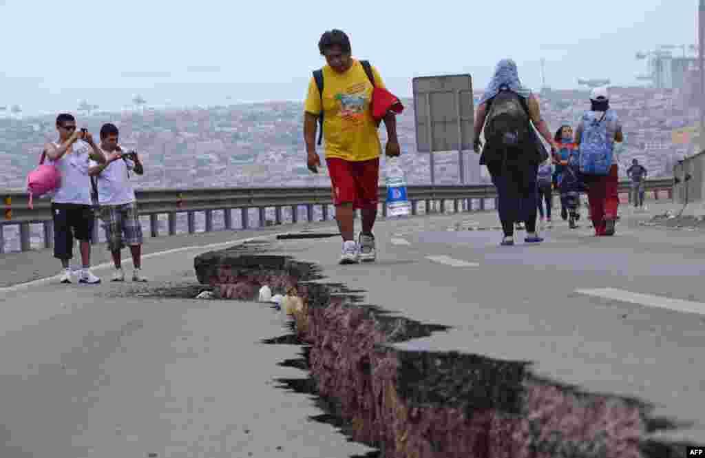 Warga Chile berjalan di sebuah jalan yang rusak akibat gempa di kota Iquique, Chile utara, sehari setelah gempa 8.2 skala Richter melanda Chile.&nbsp;