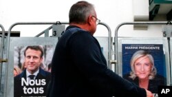 Un homme passe devant des affiches de campagne présidentielle du président français Emmanuel Macron et de l'opposante d'extrême droite Marine Le Pen à Anglet, dans le sud-ouest de la France, le 8 avril 2022.