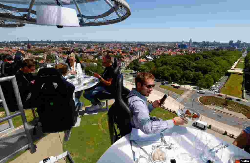 People sit at one of the eight tables on a nine-ton structure, suspended from a crane at a height of 50 meters, that can accommodate a total of thirty two guests for a meal during an event known as &quot;Dinner in the Sky&quot; outside Koekelberg Basilica in Brussels, Belgium.