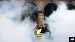 Para demonstran mengenakan rompi kuning berjalan melewati bom asap dekat taman-taman Tuileries di Paris, Sabtu, 22 Desember 2018. (Foto: AP/Kamil Zihnioglu)
