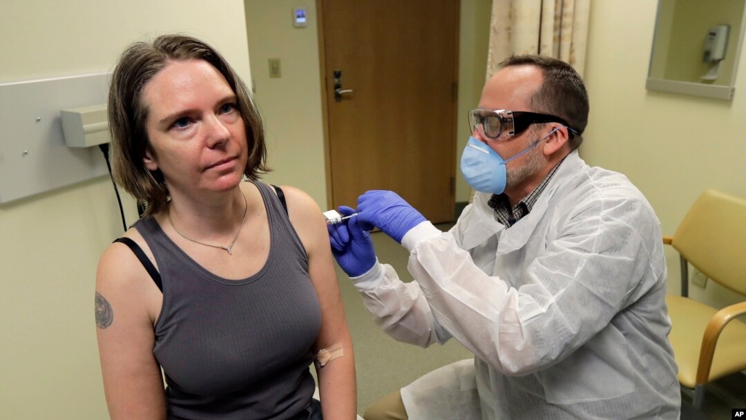 FILE - Jennifer Haller, left, receives the first shot in the first-stage safety study clinical trial of a potential vaccine for COVID-19, March 16, 2020, at the Kaiser Permanente Washington Health Research Institute in Seattle. (AP Photo/Ted S. Warren)