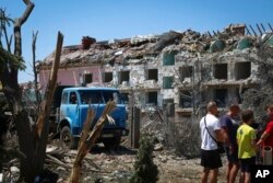 Local residents stand next to a damaged residential building in the town of Serhiivka, about 50 kilometers southwest of Odesa, Ukraine, July 1, 2022.