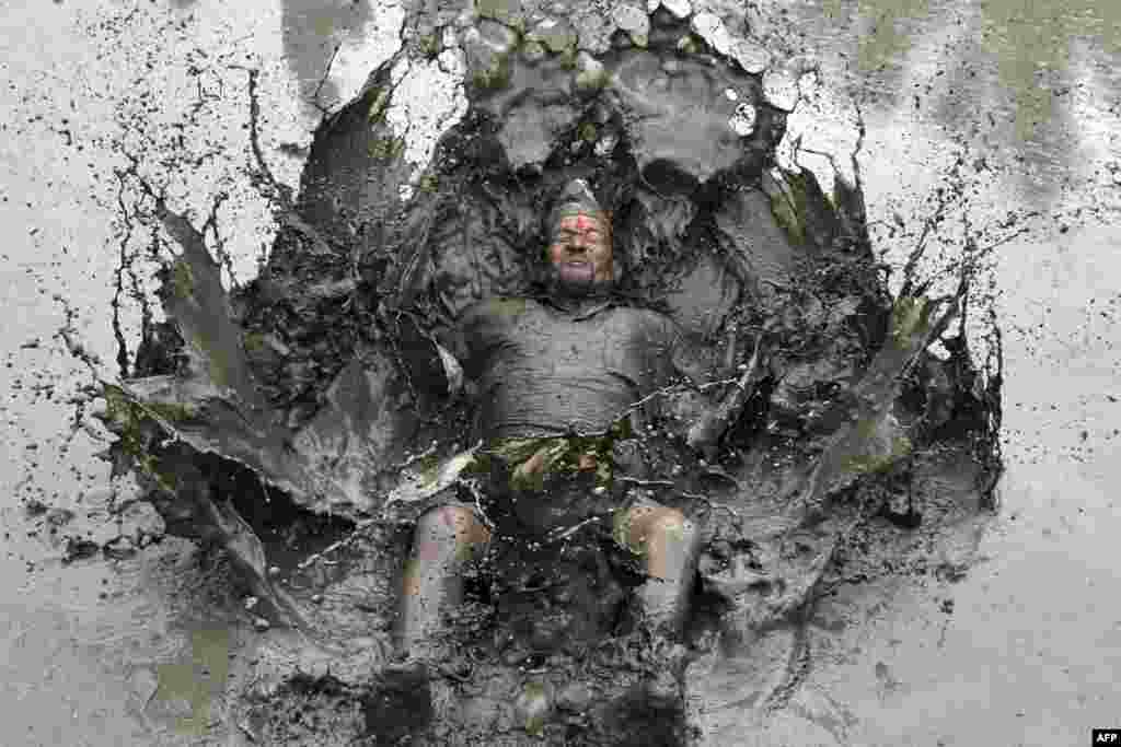 A mud-covered farmer plays in a rice paddy field during &quot;National Paddy Day,&quot; which marks the start of the annual rice planting season, in Tokha village on the outskirts of Kathmandu, Nepal.
