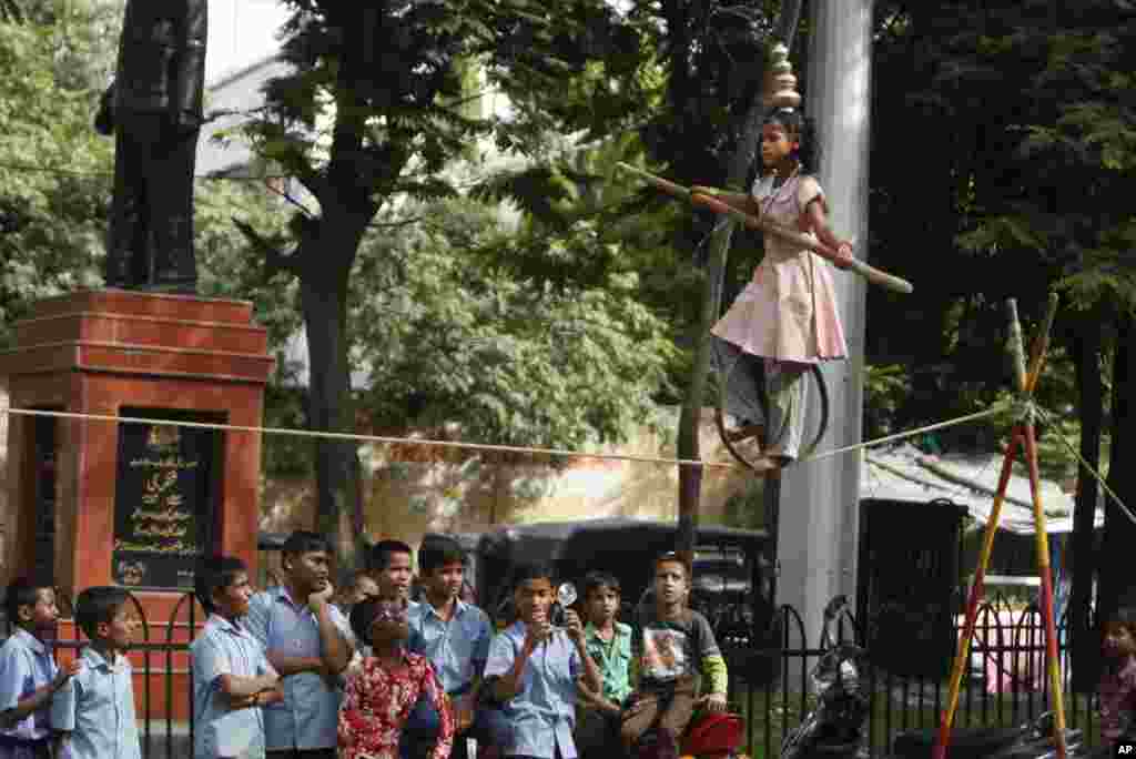 Murid-murid sekolah India menonton pertunjukan akrobat berjalan di atas tambang dari anak jalanan di Hyderabad. 