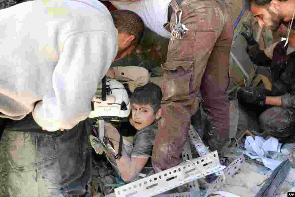 Syrian civil defense volunteers help a boy out of the rubble following an attack, reportedly by Syrian government forces, in the Tariq al-Bab neighborhood in the northern city of Aleppo.