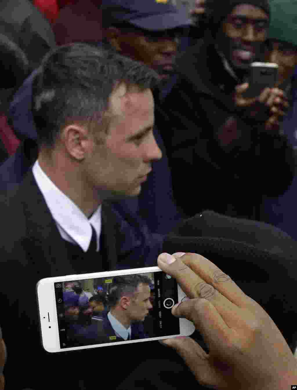 Oscar Pistorius, is escorted by police officers as members of the public take photos with their mobile phones outside the High Court in Pretoria, South Africa after his sentencing proceedings. An appeals court found Pistorius guilty of murder, and not culpable homicide for the shooting death of his girlfriend Reeve Steenkamp.