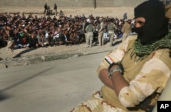 FILE - With his face covered, an Iraqi soldier sits on his humvee in front of scores of Iraqi male residents who were rounded up by Iraqi forces, in Gogjali neighborhood, in Mosul, Iraq, Nov. 24, 2016. Iraqi forces urged them to report any IS-related information.
