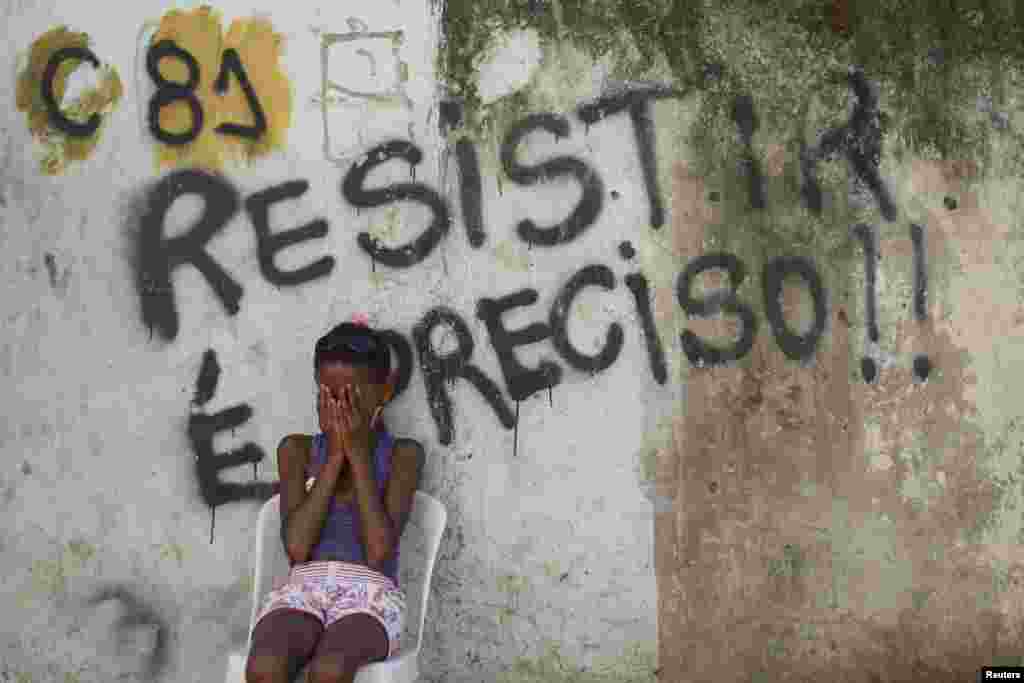 Seorang anak perempuan duduk di depan tembok dengan grafiti yang berbunyi, 'Kita harus bertahan,' di wilayah kumuh dekat Stadion Maracana di Rio de Janeiro. Warga melakukan protes atas penggusuran rumah mereka.Penggusuran warga itu merupakan bagian dari proyek renovasi untuk menyambut Piala Dunia 2014.