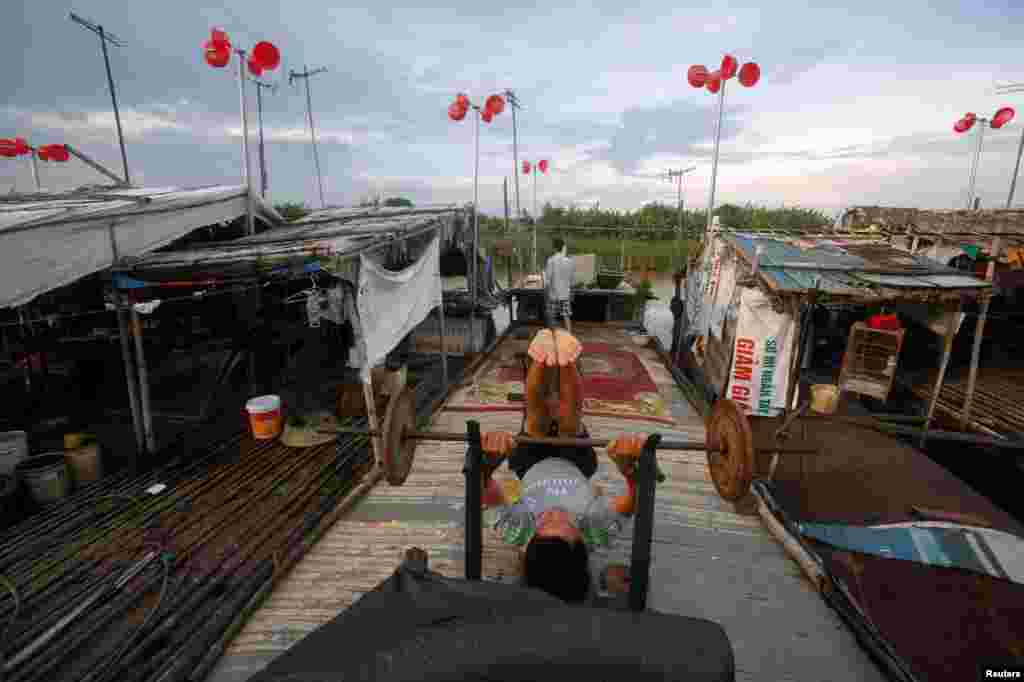 A man exercises on his boat in front of a wind power system made from plastic buckets, at a floating village in Hanoi, Vietnam.