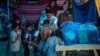 Seorang aktivis Rohingya membagikan baju baru kepada para pengungsi di sebuah kamp pengungsi di tepi Sungai Yamuna, 1 Juli 2021. (Foto: AP/Altaf Qadri)