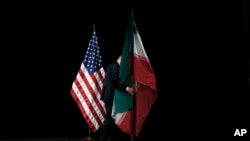 Seorang petugas membereskan bendera Iran yang terpasang di panggung di Vienna International Center, yang menjadi tempat perundingan nuklir Iran, pada 14 Juli 2015. (Foto: Pool via AP/Carlos Barria)