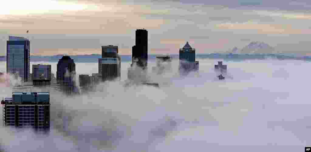 Gedung-gedung di pusat kota tampak di antara kabut pagi sementara terlihat di kejauhan,&nbsp; sekitar 80 mil, adalah Gunung Rainier, seperti terlihat dalam foto ini yang diambil dari dari atas Space Needle di Seattle. &nbsp;