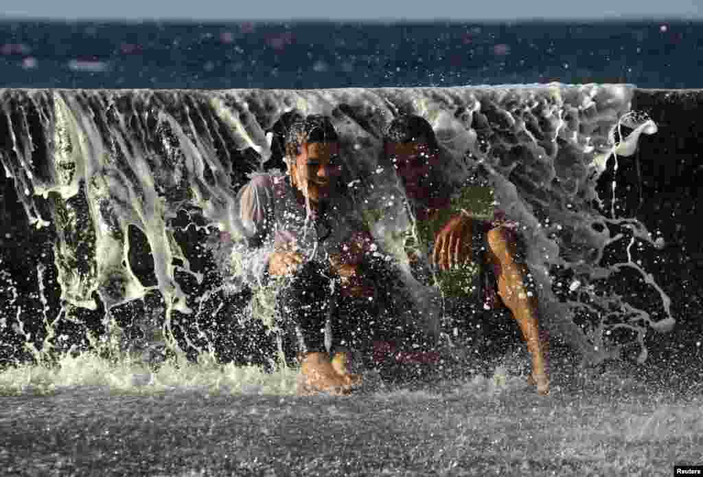 Sepasang muda-mudi tertawa saat gelombang laut menghantam mereka di pantai 'El Malecon', Havana, Kuba.