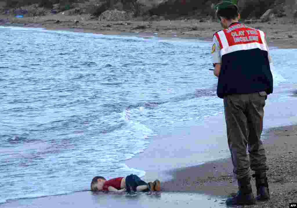 A Turkish police officer stands next to a migrant child's dead body (Aylan Shenu) off the shores in Bodrum, southern Turkey, on Sept. 2, 2015 after a boat carrying refugees sank while reaching the Greek island of Kos.