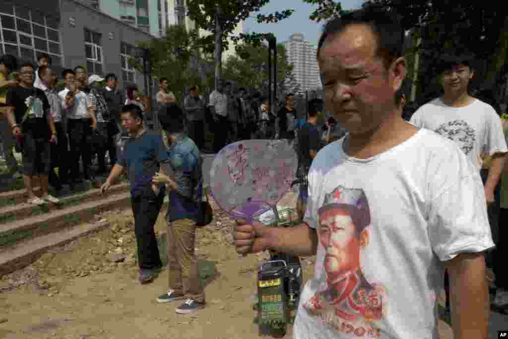 A man wearing a t-shirt with a picture of former Chinese leader Mao Zedong holds a fan with the words "Bo Xilai" near the Jinan Intermediate People's Court in Jinan, August 22, 2013.