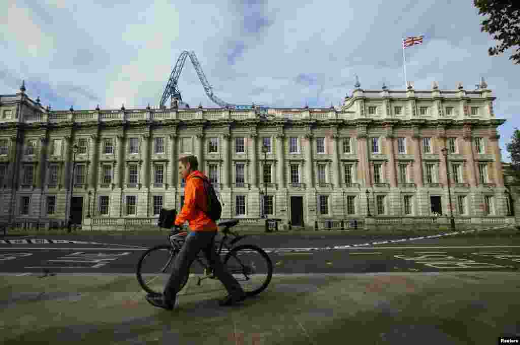 A cyclist pushes his bicycle past the Cabinet Office with a collapsed crane on its roof in London, Oct. 28, 2013.