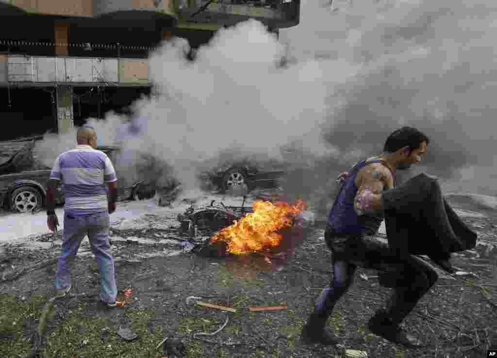 A Lebanese man runs in front of a burned car, at the scene of two explosions near the Iranian Embassy in Beirut, Lebanon. The blasts in south Beirut's neighborhood of Janah killed more than 20 people and caused extensive damage on the nearby buildings and the Iranian mission.