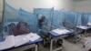 FILE - A woman holds her son, suffering from dengue fever, as she sits under a mosquito net inside a dengue ward of a local hospital in Rawalpindi, Pakistan.