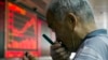 A Chinese investor uses a magnifying glass to look at his mobile phone screen as he monitors stock prices at a brokerage house in Beijing, China, July 9, 2015. 