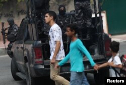 Residents walk past police officers during an operation after clashes with drug dealers in Vidigal slum in Rio de Janeiro, Aug. 14, 2018.