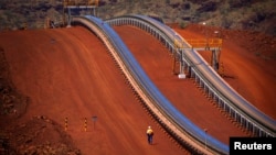 FILE - A worker walks near conveyer belts loaded with iron ore at the Fortescue Solomon iron ore mine located in the Valley of the Kings, around 400 km (248 miles) south of Port Hedland in the Pilbara region of Western Australia.