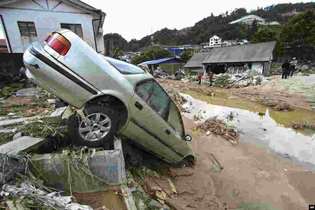 People stand near a car destroyed by a mud slide in Cameron Highlands, Malaysia. Several people were killed after water released from a dam caused a flash flood in the resort area, according to local sources.