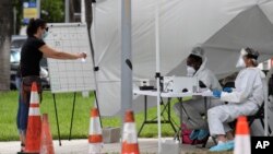 Health care workers take information from people in line at a walk-up COVID-19 testing site during the coronavirus pandemic, July 17, 2020, in Miami Beach, Fla. 
