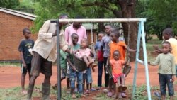 As children wait their turn on a swing set, Kanduwa Sande give one a push. (Lameck Masina/VOA)