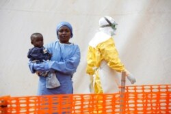 FILE - Mwamini Kahindo, an Ebola survivor working as a caregiver to babies who are confirmed Ebola cases, holds an infant outside the red zone at the Ebola treatment center in Butembo, DRC, March 25, 2019.