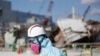 FILE - A Tokyo Electric Power Co. (TEPCO) employee, wearing a protective suit and a mask, walks in front of the No. 1 reactor building at the tsunami-crippled Fukushima Dai-ichi nuclear power plant in Okuma, Fukushima Prefecture, northeastern Japan, Wedne