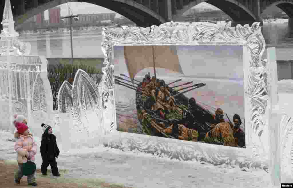 Children walk past a reproduction of a creation by Russian classical painter Vasily Surikov called "The Magical Ice of the Siberia" - which is on display in an ice frame - before the opening of the 2nd International Festival of Snow and Ice Sculpture, on the bank of the Yenisei River in Krasnoyarsk.