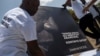 Des hommes placent un portrait du défunt président haïtien Jovenel Moïse avec une citation de lui qui se lit en créole "J'ai essayé, n'abandonnez pas. Continuez la bataille" à un mémorial devant le Palais présidentiel, à Port-au-Prince, Haïti le 14 juillet 2021.