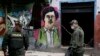 FILE - Police officers stand in front of a mural depicting the late drug kingpin Pablo Escobar, in the area known as El Bronx in downtown Bogota, Colombia, May 30, 2016. The area has been plagued by drug addicts and prostitution, including girls forced into sexual servitude.
