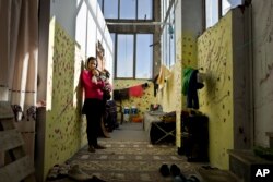 FILE - Parvaine Haideri, 30 and 5 months pregnant, an Afghan refugee from Kandahar, holds her 17-month old daughter Nazanin, while posing for a picture by the entrance of her shelter at the refugee camp of Oinofyta, Greece, Dec. 26, 2016.