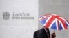 FILE - A worker shelters from the rain as he passes the London Stock Exchange in the City of London at lunchtime, Oct. 1, 2008. 