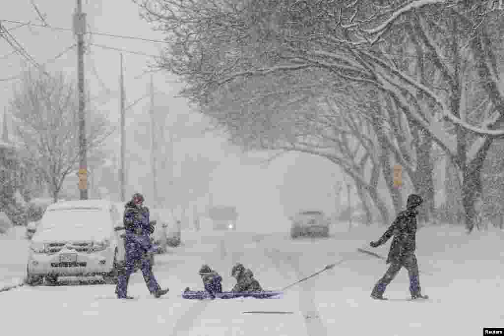 Laura Dejong pulls her nephews Caleb and Eli Fennema while their mother follows behind with infant Grace during a snow fall in Hamilton, Ontario, Canada, Jan. 25, 2023. 