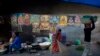An Indian woman sweeps a pavement past a wall covered with posters of Hindu Gods in Gauhati, India, Monday, Jan. 2, 2017.