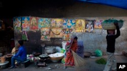 An Indian woman sweeps a pavement past a wall covered with posters of Hindu Gods in Gauhati, India, Monday, Jan. 2, 2017.