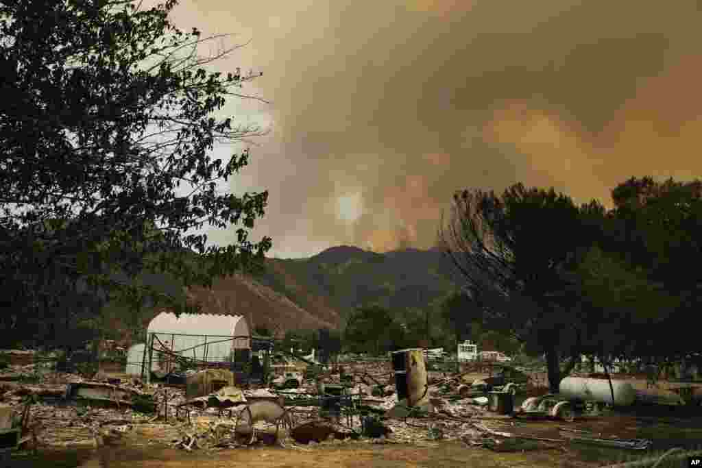 The remains of mobile homes devastated by a wildfire are seen in the foreground as smoke rises over a mountain in South Lake, California, June 25, 2016.