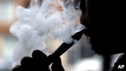 FILE - A person inhales and exhales vapor from an electronic cigarette.